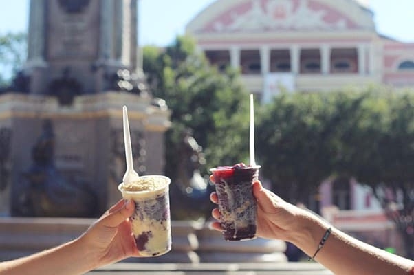 Deux personnes tiennent des coupes d’açaí devant le théâtre Amazonas à Manaus.