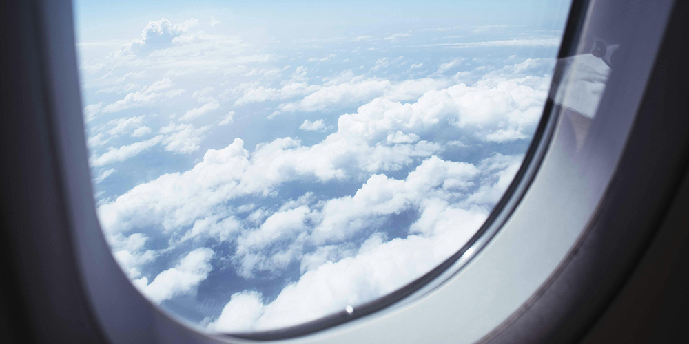 Vue paisible depuis un hublot d’avion, montrant un ciel bleu clair parsemé de nuages blancs cotonneux.