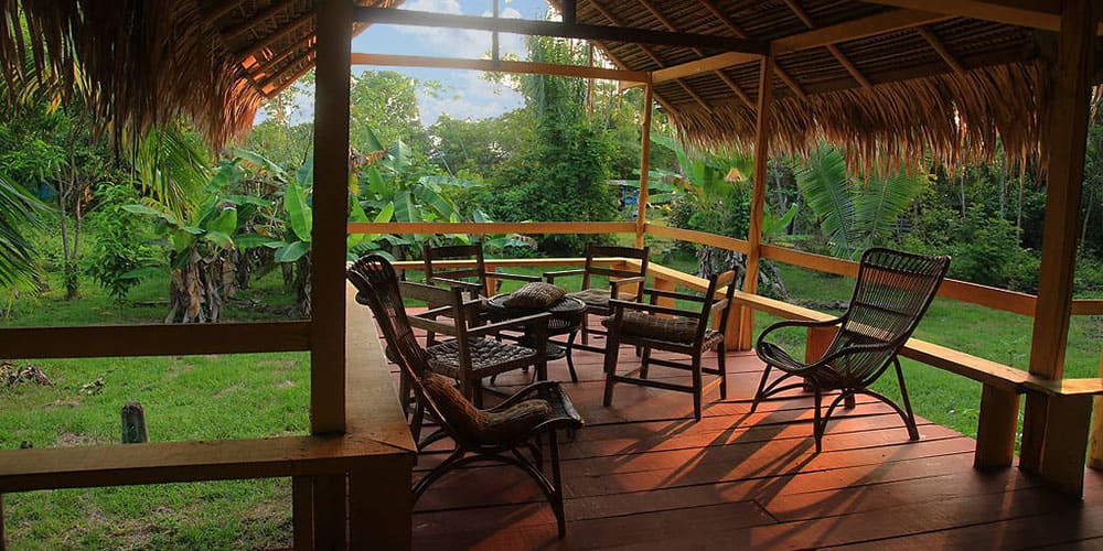 Terrasse en bois avec fauteuils sous un toit de palmes, entourée de végétation tropicale.