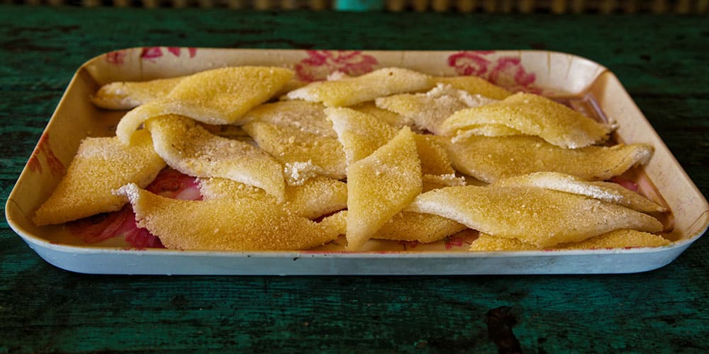 Plateau de galettes de tapioca artisanaux, dorés et croustillants, disposés sur un plateau en métal à fleurs.