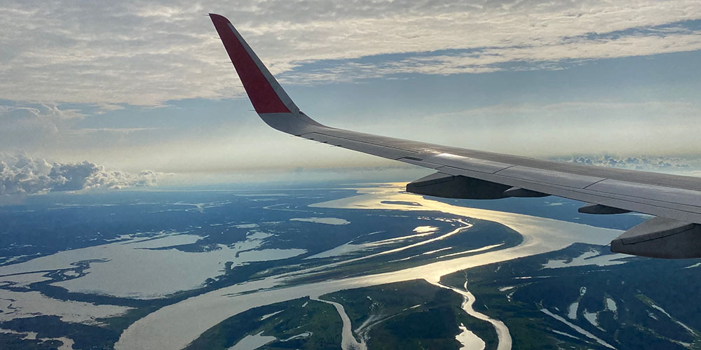 Vue depuis le hublot d’un avion en vol, montrant une large portion du fleuve Amazone serpentant entre les forêts, baignée par la lumière dorée du soleil couchant.