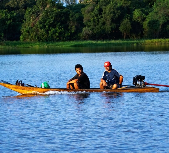 Deux hommes naviguant sur une pirogue motorisée dans les eaux calmes de l’Amazone