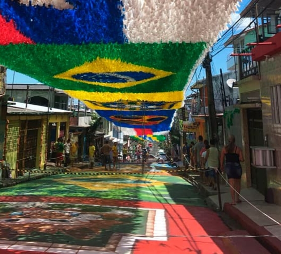 Une rue en pente est ornée de guirlandes colorées suspendues, formant le drapeau du Brésil, avec le sol également peint de motifs festifs.