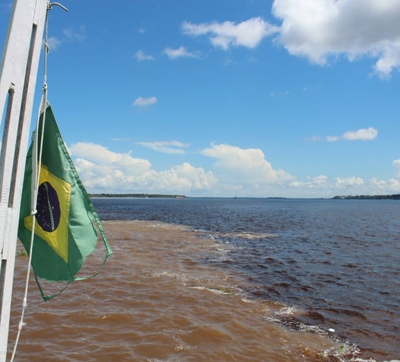 Photo prise depuis un bateau montrant le phénomène naturel de la “Rencontre des eaux” à Manaus, où les eaux sombres du Rio Negro et les eaux claires du Rio Solimões se rejoignent sans se mélanger immédiatement.