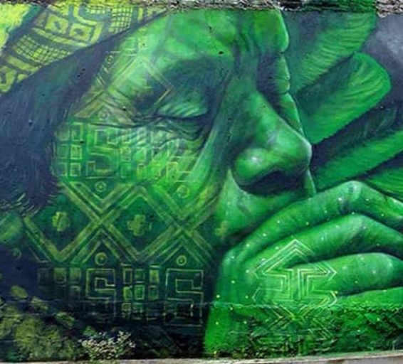 Portrait mural d’un visage chamanique en vert, yeux fermés, soufflant à travers un tuyau ou une pipe.