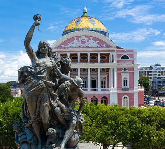Statue devant le Théâtre Amazonas à Manaus, avec son dôme coloré et façade rose emblématique.