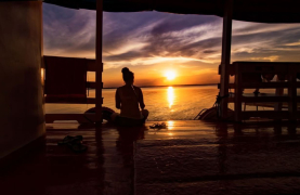 Silhouette d’une personne assise sur un bateau observant un coucher de soleil sur le fleuve