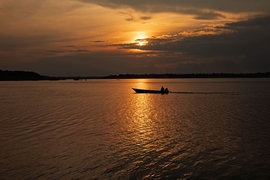 Une pirogue avance sur un fleuve calme au coucher du soleil, reflétant la lumière dorée